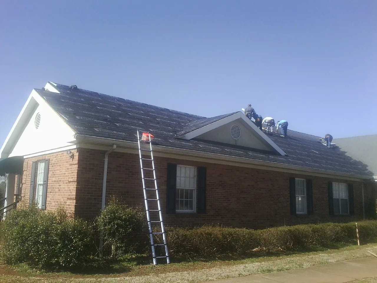 Crew tearing shingles off a brick ranch roof with a ladder set — Emergency Roof Repair work by our crew in Cherokee