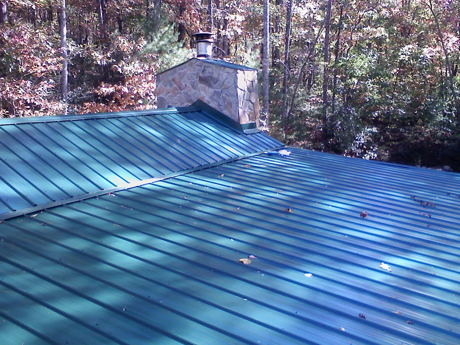 New green metal roof and stone chimney surrounded by autumn woods in Cherokee