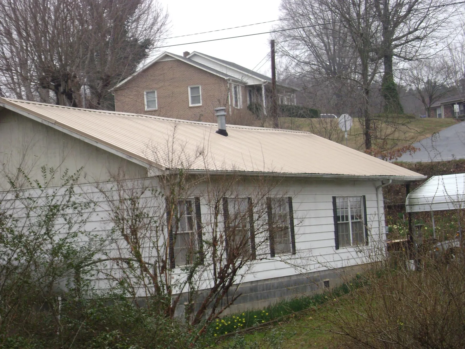 Tan metal roof on a white sided house set into a hillside — Commercial Roofing by Roofing Brothers in Cherokee