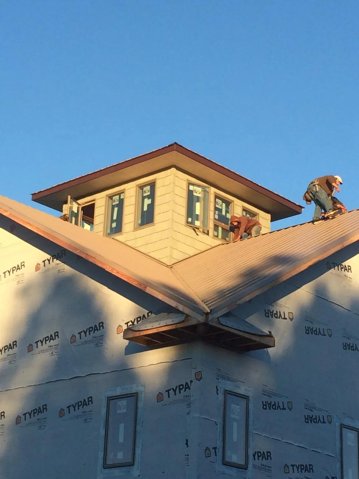 Roofers working around a rooftop cupola on a new metal roof at sunset — Roof Waterproofing in Cherokee by Roofing Brothers